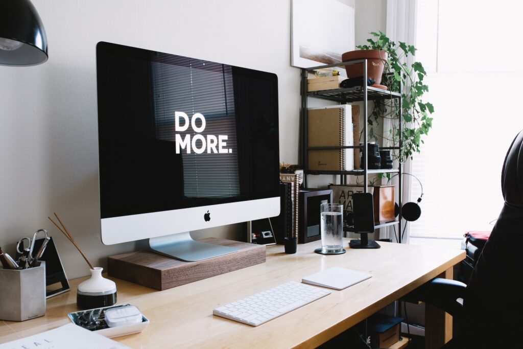 Desk with large Apple computer monitor displaying "Do More"