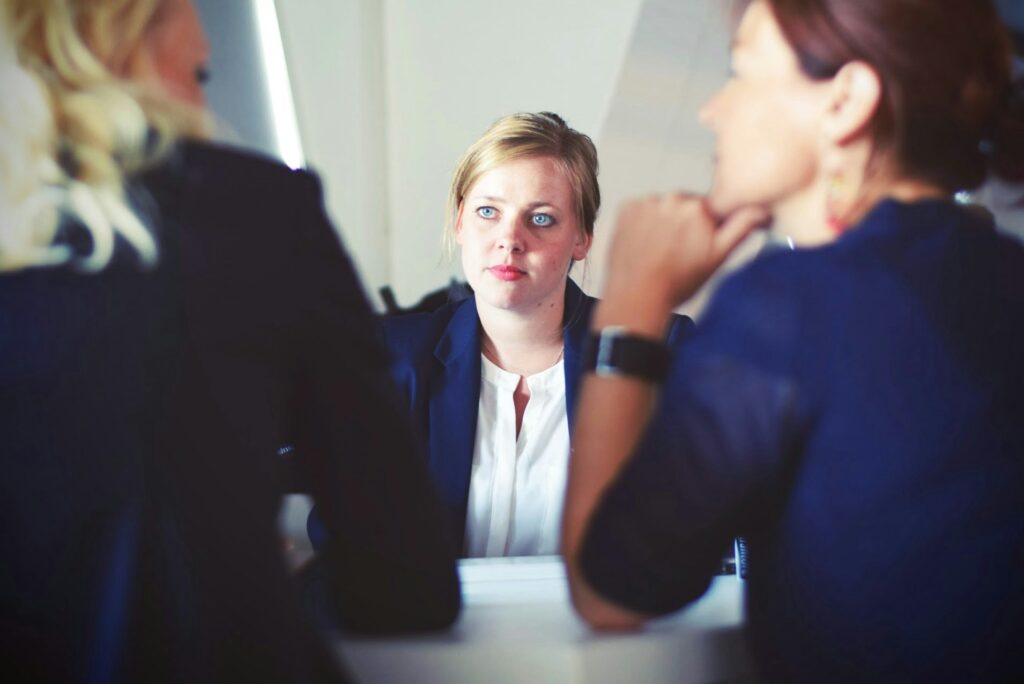 A professional woman in a navy blue blazer is engaged in a serious conversation with two other individuals in a business setting